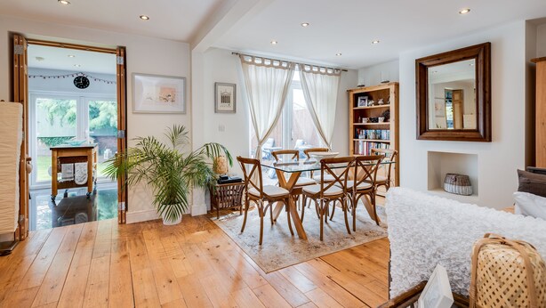 A spacious room with wooden flooring, a dining area with a glass table and wooden chairs, a bookshelf, and a large mirror. - Headington Orchard - 3 Bedroom House & parking & garden (Oxford)