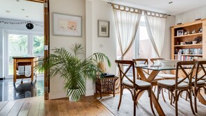 A dining area with a glass table and wooden chairs, a potted plant, and a bookshelf with books and decorative items. - Headington Orchard - 3 Bedroom House & parking & garden (Oxford)