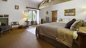 A bedroom with a large bed, a desk, a chair, and a window with curtains.