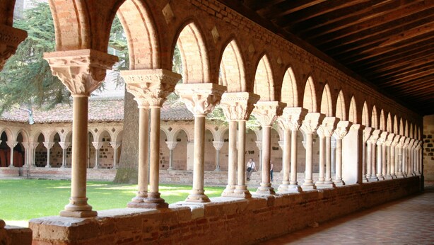 A corridor with a series of arches supported by columns, leading to a courtyard with a grassy area and trees.