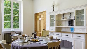A dining area with a table set for breakfast, including bowls, plates, and a coffee pot. There are chairs around the table, and a cabinet with glass doors and shelves to the right.