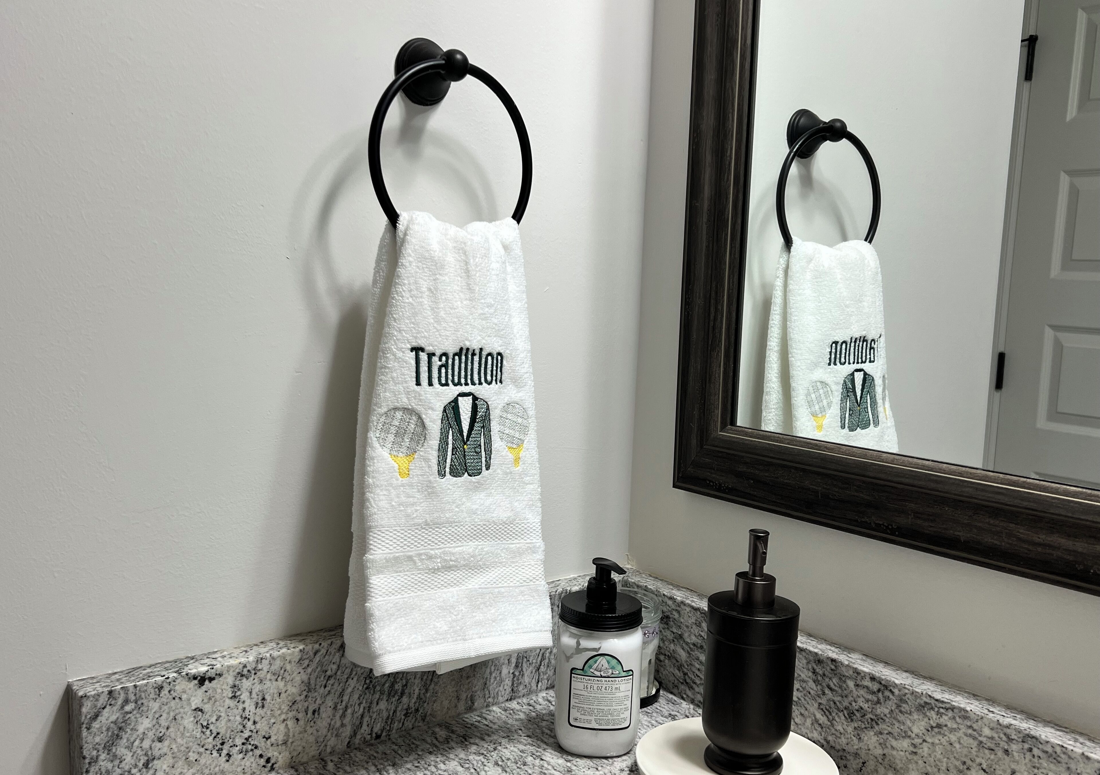 A bathroom with a towel hanging on a ring, a bottle of hand soap, and a black pump dispenser on the counter.