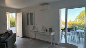 Un salon moderne avec un canapé, un bureau blanc et une porte en verre donnant sur un espace extérieur.
