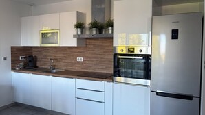 Une cuisine moderne avec des meubles blancs, un réfrigérateur en acier inoxydable, un four encastré et une machine à café.