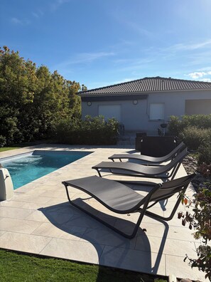 Una piscina con sillas de descanso, una parrilla y una casa con techo de tejas.