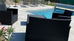 Un espace aménagé au bord de la piscine, avec des meubles en osier, un parasol et une vue sur la piscine.