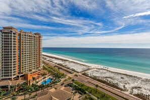 A high-rise hotel with a beach view, a swimming pool, and a road leading to the beach.