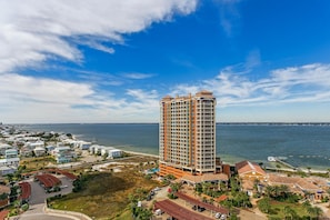 A high-rise hotel with multiple balconies, a parking area, and a view of the ocean.