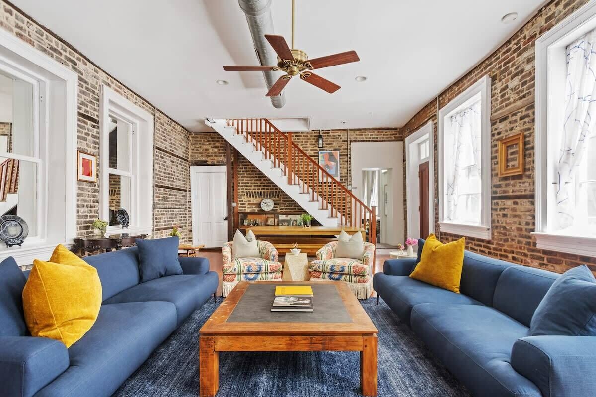 A spacious living room with a brick wall, a wooden coffee table, blue sofas, and a staircase leading to another level.