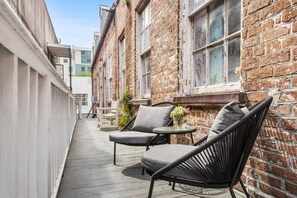 En smal udendørs passage med træterrasse, to fletstole, et lille rundt bord og en potteplante.