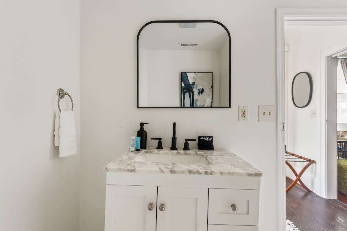 A bathroom with a white vanity, a black-framed mirror, and a white towel hanging on the wall.