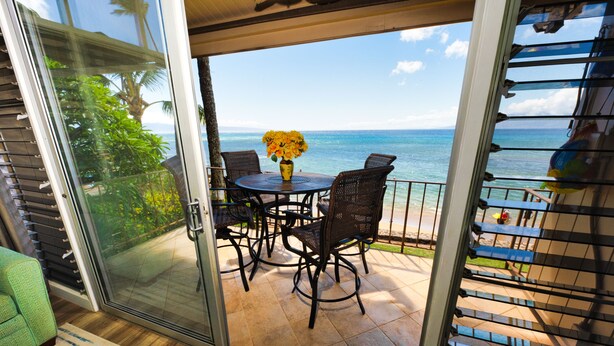 Een schuifdeur die uitkomt op een terras met een ronde tafel en stoelen, een vaas met gele bloemen en uitzicht op de oceaan.