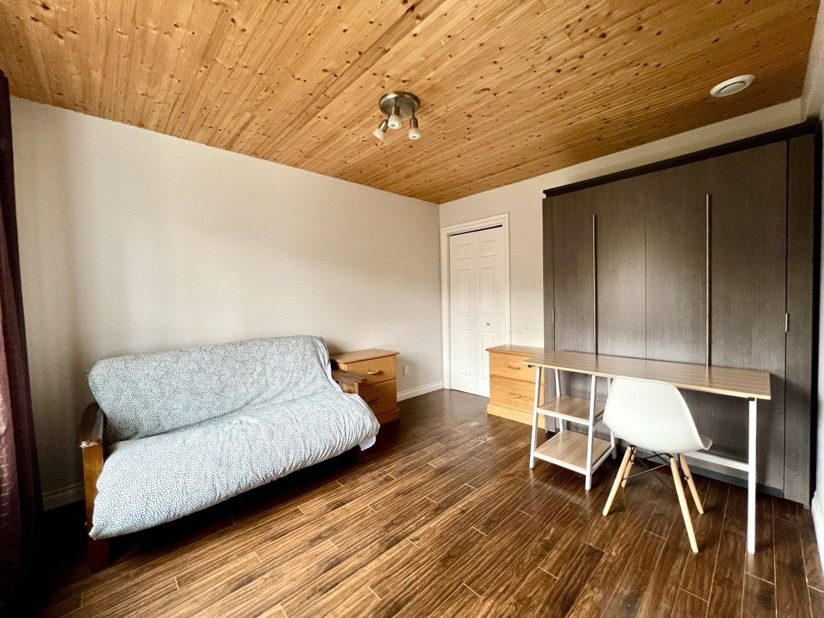 A room with a wooden ceiling, a sofa, a desk, and a wardrobe.