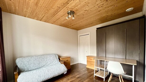 Ein Zimmer mit Holzbalkendecke, einer Couch, einem Schreibtisch und einem Kleiderschrank.