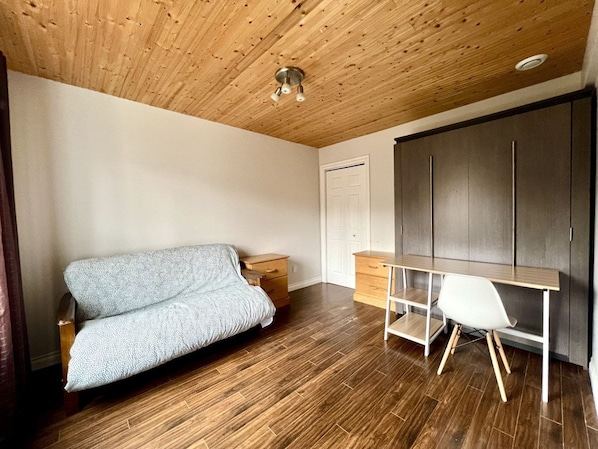 A room with a wooden ceiling, a sofa, a desk, and a wardrobe.