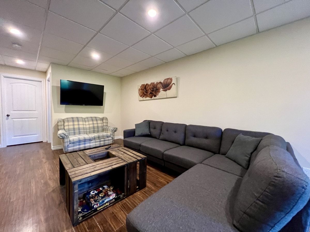 A living room with a sofa, a plaid chair, a coffee table, and a flat-screen TV mounted on the wall.