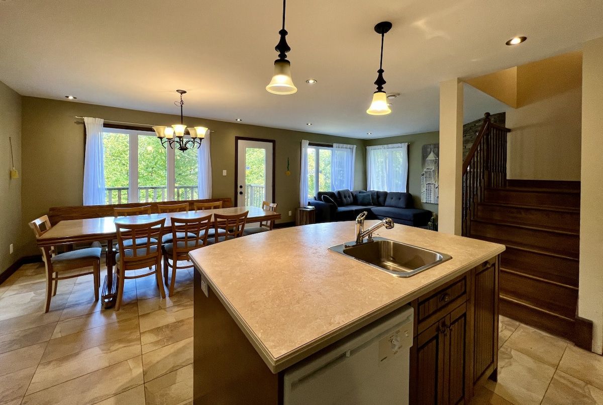 A spacious kitchen with a central island, dining area with wooden chairs, and a staircase leading to a loft.