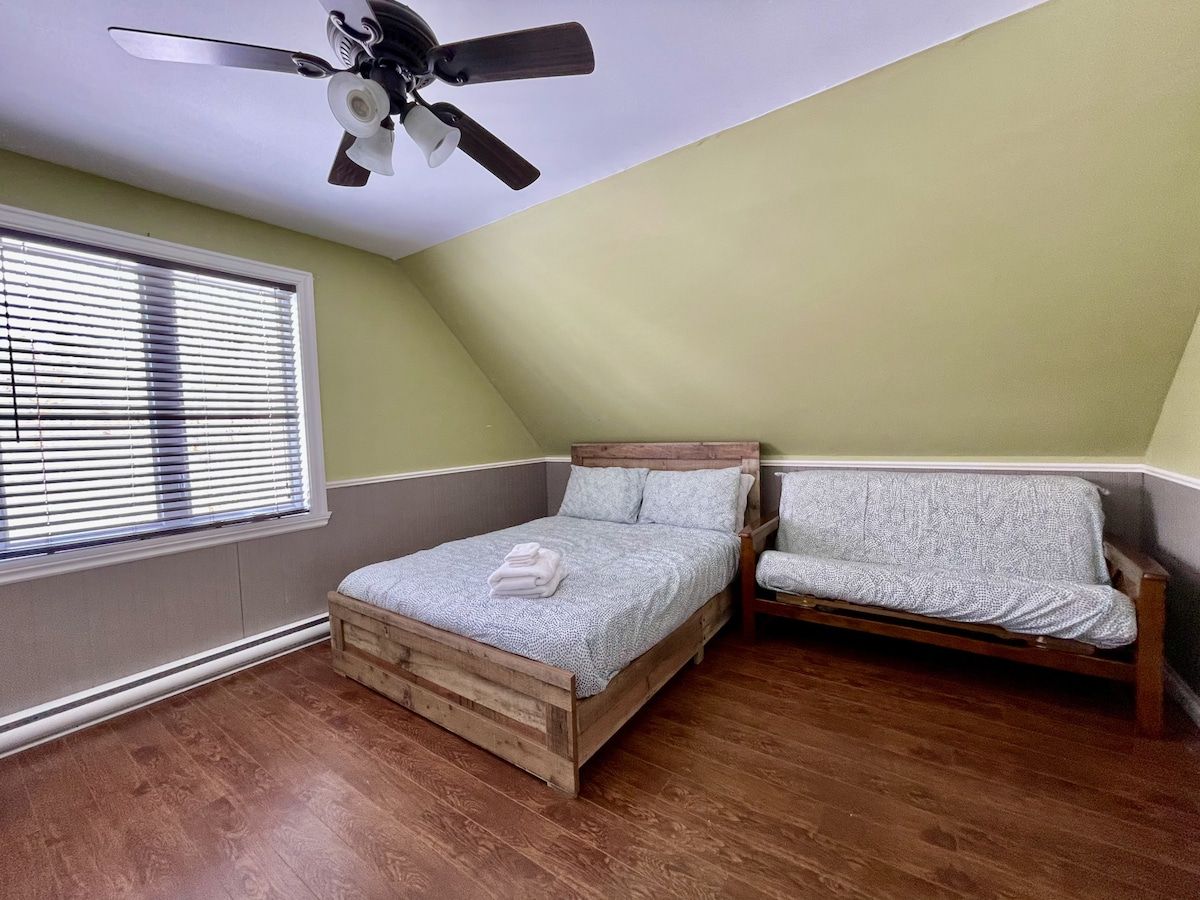 Ein Schlafzimmer mit schrägem Dach, einem Bett, einer Bank und einem Deckenventilator.