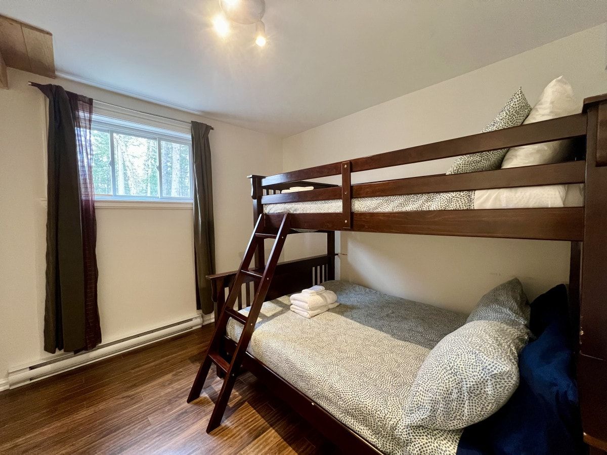 A bunk bed with a ladder, a window with curtains, and a wooden floor.
