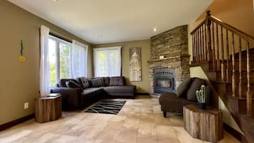A living room with a sectional sofa, a fireplace, a staircase, and a view of trees through the windows.
