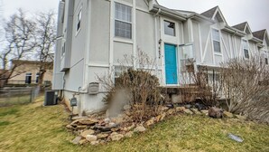 A two-story house with a blue front door, a stone foundation, and a small garden area with rocks and sparse grass. - Beautiful, spacious, clean house for families #1 (Overland Park)