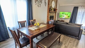 A dining area with a wooden table, chairs, and a bench. There is a fireplace with a clock above it, and a television on the wall. - Beautiful, spacious, clean house for families #1 (Overland Park)