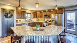 A kitchen with granite countertops, wooden cabinets, stainless steel appliances, and pendant lighting. - Annie Creek Lodge – Hot tub, game loft, fireplaces & stunning views! (Lead)