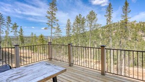 A wooden deck with a metal railing, overlooking a forested area. - Annie Creek Lodge – Hot tub, game loft, fireplaces & stunning views! (Lead)