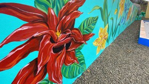 Een levendige muurschildering met grote rode bloemen en groene bladeren op een turquoise muur.
