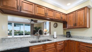A kitchen with wooden cabinets, a granite countertop, a dishwasher, and a view of the outdoors.
