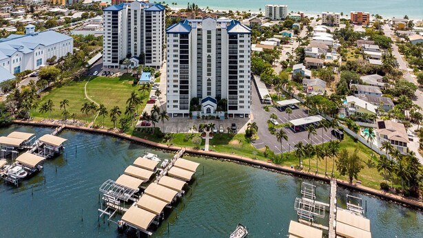 A high-rise hotel with multiple floors, a marina with boats, and a beach in the background.