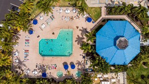 An aerial view of a resort with a central swimming pool, sun loungers, and palm trees.