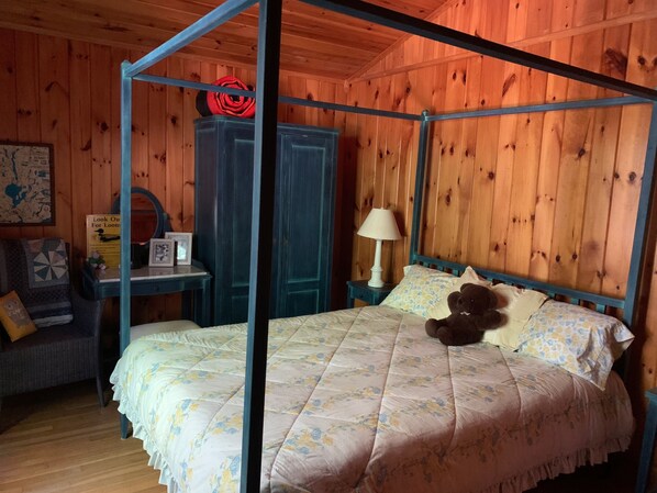 A four-poster bed with floral bedding, a bedside lamp, and a teddy bear.