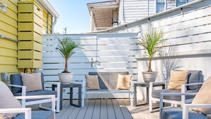 Una terraza con mobiliario blanco, incluyendo sofás y un banco, rodeada de plantas en macetas.