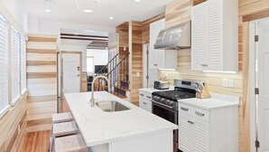 Una cocina moderna con una isla central, detalles de madera, armarios blancos y una campana extractora de acero inoxidable.