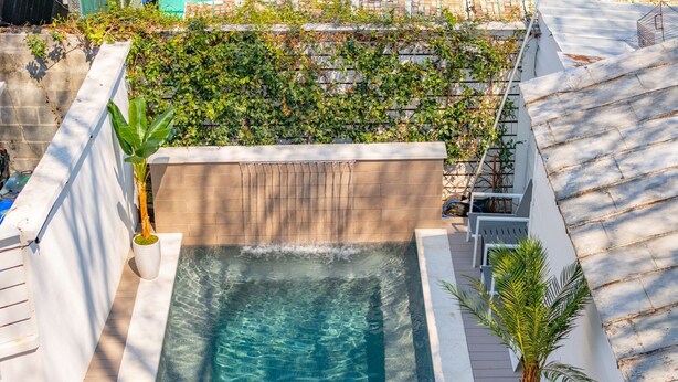 Una piscina en la azotea con dos sillas de descanso y una palmera.