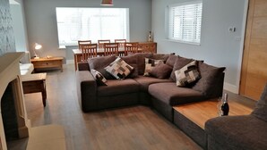 A modern living room with a sectional sofa, wooden flooring, and a dining area with a table and chairs. - House with 5 Double bedrooms including large family room,4 Bathrooms, Gym &patio (Brough)