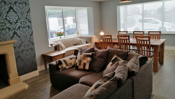 A living room with a sofa, a dining table with chairs, a fireplace, and large windows with blinds. - House with 5 Double bedrooms including large family room,4 Bathrooms, Gym &patio (Brough)