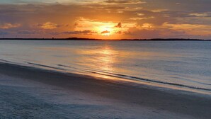 Cena de praia com o pôr do sol refletindo na água.