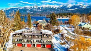 A multi-story building with balconies, a parking area, and a view of mountains and a lake. - On The River | Hot Tub | Fire Pit | Upgraded AC! (Whitefish)