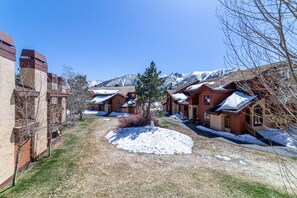 Houses with pitched roofs line a quiet street, surrounded by snow-covered trees and snow-capped mountains.