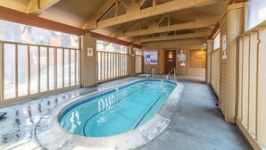 En inomhuspool med träbjälkar, glasräcken och varningsskyltar.