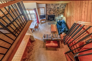 Un vaste salon doté d’une cheminée en pierre, d’un canapé bleu et d’un escalier en bois.