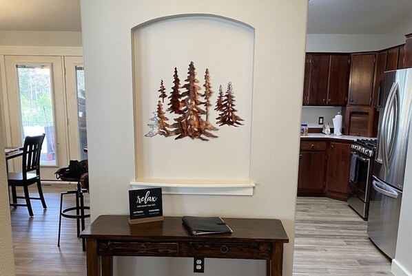 A modern kitchen with wooden cabinets, a stainless steel refrigerator, and a dining area with a table and chairs. - Timbercrest Retreat - Delightful Home near river, Couer d'Alene & Silverwood! (Post Falls)