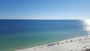 Une plage avec une eau d’un bleu limpide et un rivage sablonneux. On y voit des parasols et des gens.