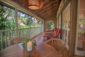 Relax in this serene outdoor space with a wooden table, wicker chairs, and a view of lush greenery.