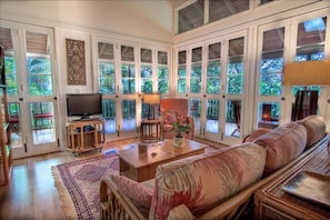 Relax in this spacious living room with a high ceiling and large windows offering a tropical view.