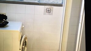 Een compacte badkamer met een wasmachine, douche en betegelde vloer.