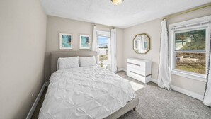 A bedroom with a large bed, a bedside table, a dresser, and a window with a view. - Tremont! 7 min to downtown Cle (Cleveland)