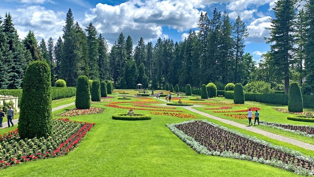 A well-maintained garden with neatly trimmed hedges and flower beds, surrounded by tall trees. - Blackhawk 5BD Home: Hot Tub, Arcade, near Whitworth & Green Bluff (Spokane)